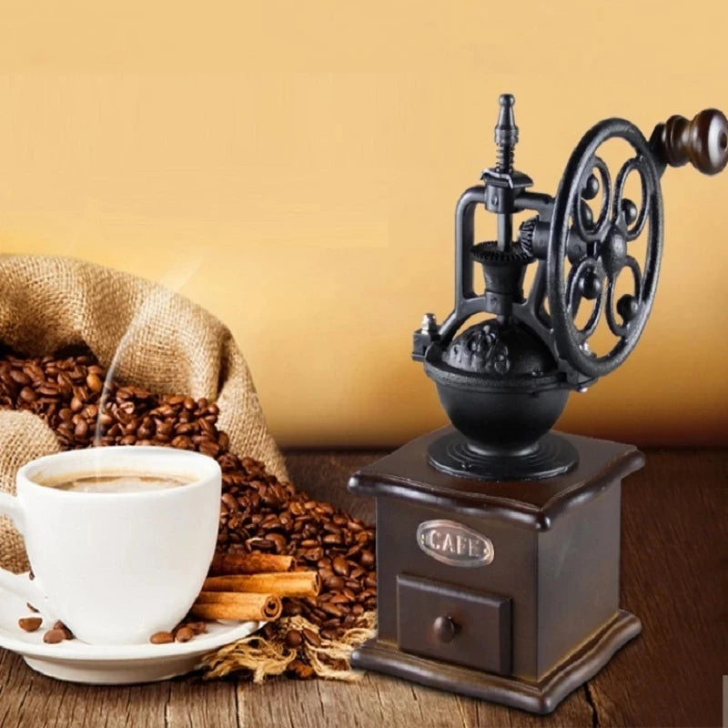 Vintage manual coffee grinder with ornate cast-iron wheel beside a cup of coffee and coffee beans on a warm background