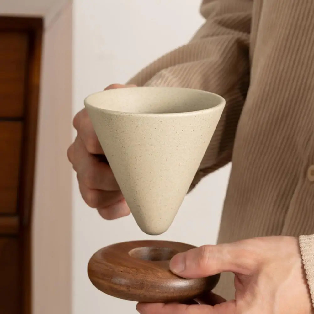 Hands separating a conical ceramic mug from its round wooden saucer base"