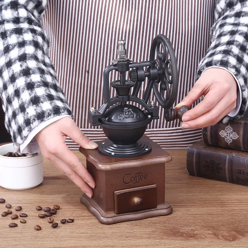 Person using a manual coffee grinder with coffee beans on a wooden surface