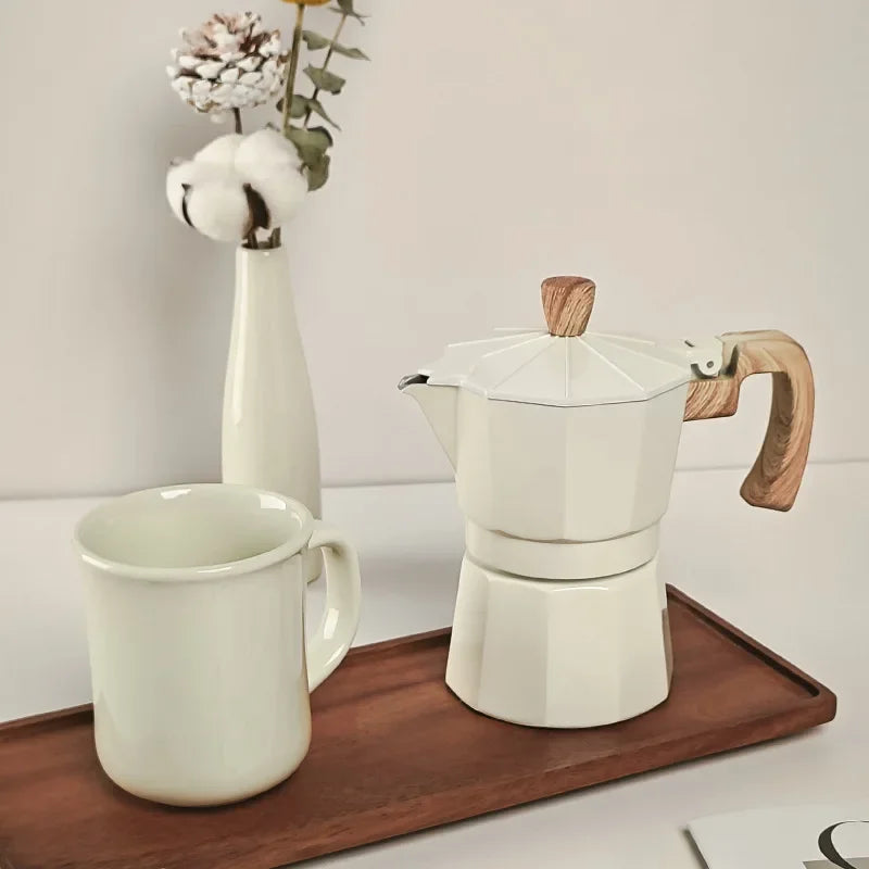 White ceramic coffee maker with wooden handle and cup on a wooden tray against a light background