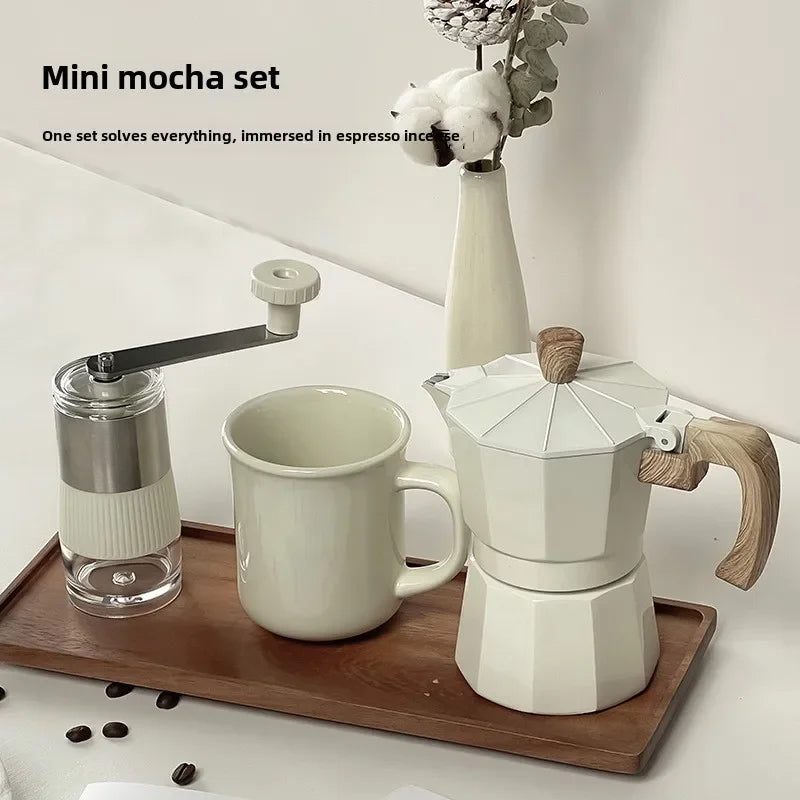 Mini mocha set with coffee grinder, mug, and stovetop espresso maker on a wooden tray.