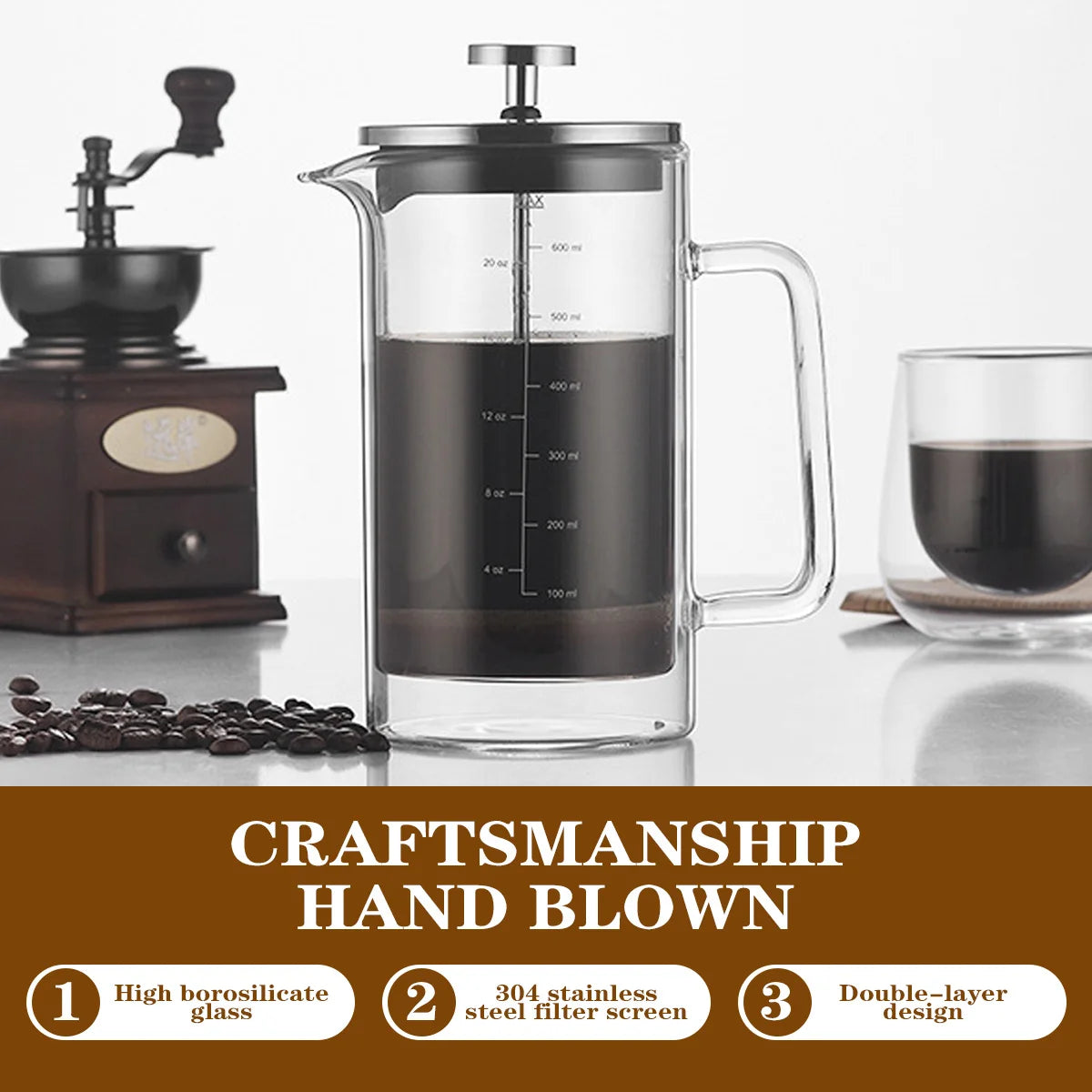 A clear glass French press coffee maker with a stainless steel plunger and handle, filled with black coffee, shown on a white surface with a coffee grinder, coffee beans, and a glass of coffee. A brown banner at the bottom reads 'CRAFTSMANSHIP HAND BLOWN' with three feature callouts.