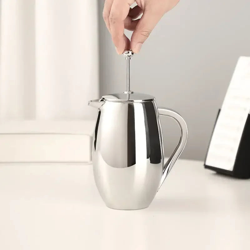 Stainless steel french press pitcher with a hand holding the handle on a light background