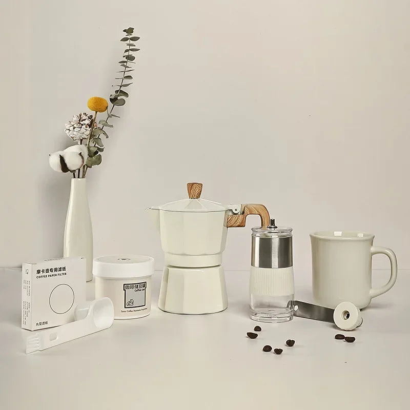 Coffee-making setup with a Moka pot, coffee beans, and a mug on a light surface.