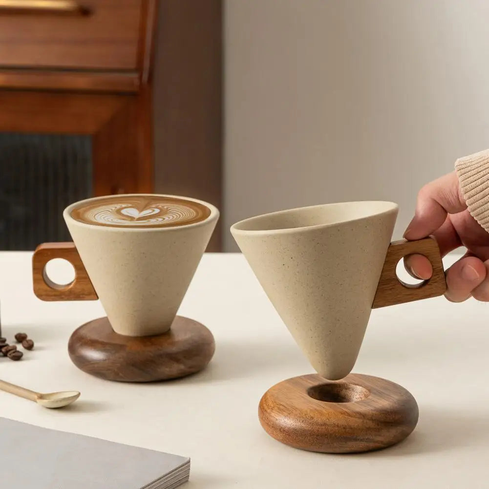 Two conical ceramic coffee mugs with wooden handles and saucer bases, one filled with latte art, on a white surface