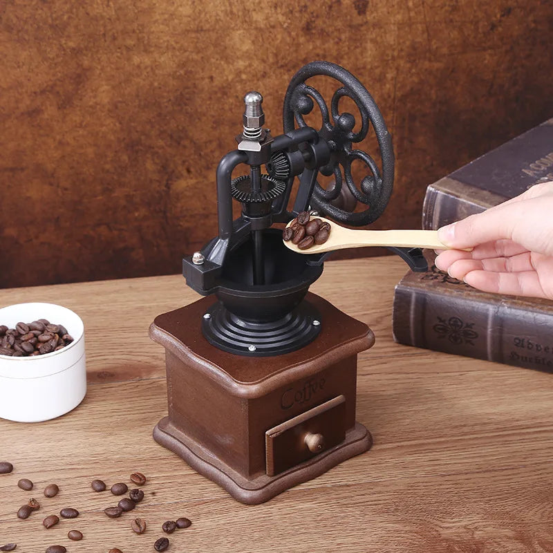 Hand holding a wooden coffee grinder with coffee beans on a wooden surface.